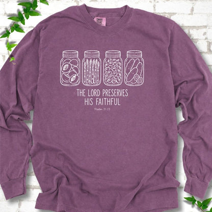 Berry long sleeve T-shirt flat lay with white line-art illustrations of four mason jars filled with peaches, asparagus, blueberries and pickles above the words "The Lord Preserves His Faithful" and small "Psalm 31:23", on white brick with ivy sprigs.
