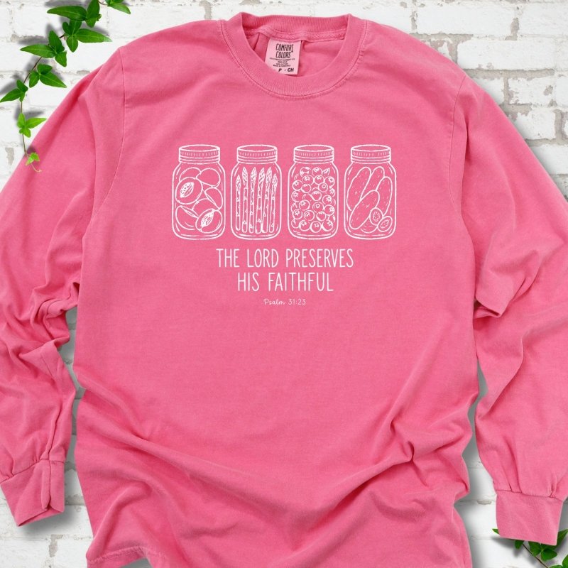Crunchberry long sleeve T-shirt flat lay with white line-art illustrations of four mason jars filled with peaches, asparagus, blueberries and pickles above the words "The Lord Preserves His Faithful" and small "Psalm 31:23", on white brick with ivy sprigs.