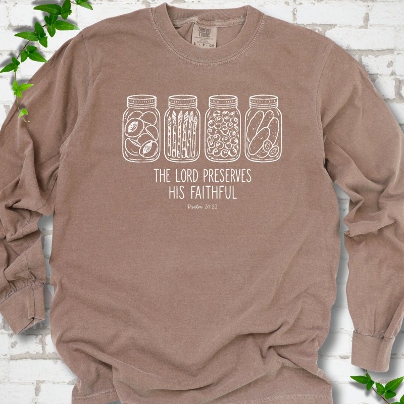 Espresso long sleeve T-shirt flat lay with white line-art illustrations of four mason jars filled with peaches, asparagus, blueberries and pickles above the words "The Lord Preserves His Faithful" and small "Psalm 31:23", on white brick with ivy sprigs.