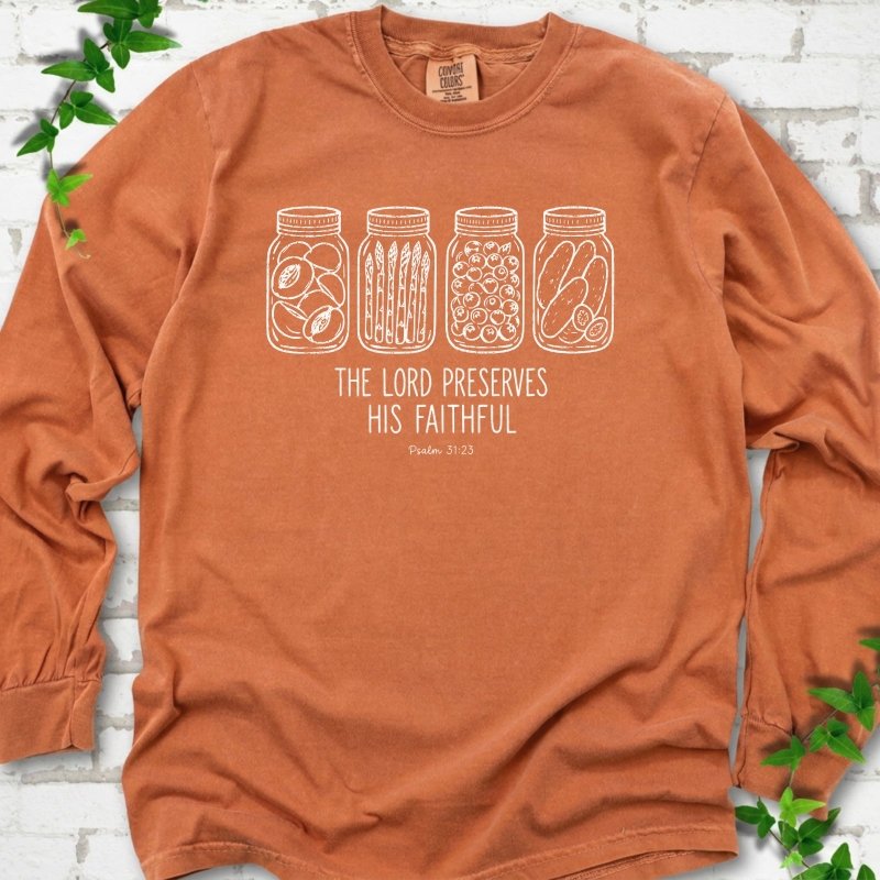 Yam long sleeve T-shirt flat lay with white line-art illustrations of four mason jars filled with peaches, asparagus, blueberries and pickles above the words "The Lord Preserves His Faithful" and small "Psalm 31:23", on white brick with ivy sprigs.