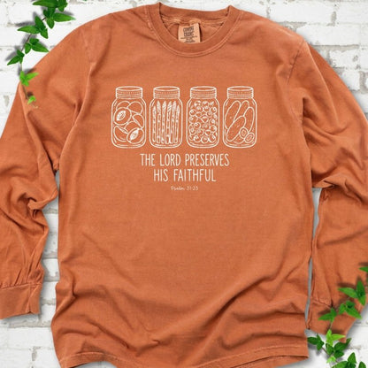 Yam long sleeve T-shirt flat lay with white line-art illustrations of four mason jars filled with peaches, asparagus, blueberries and pickles above the words "The Lord Preserves His Faithful" and small "Psalm 31:23", on white brick with ivy sprigs.