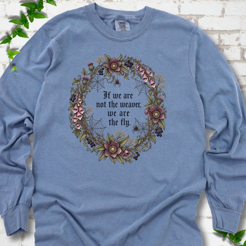 Blue Jean long sleeve T-shirt flat-lay mockup with a gothic floral wreath, spider webs and "If we are not the weaver, we are the fly" lettering.