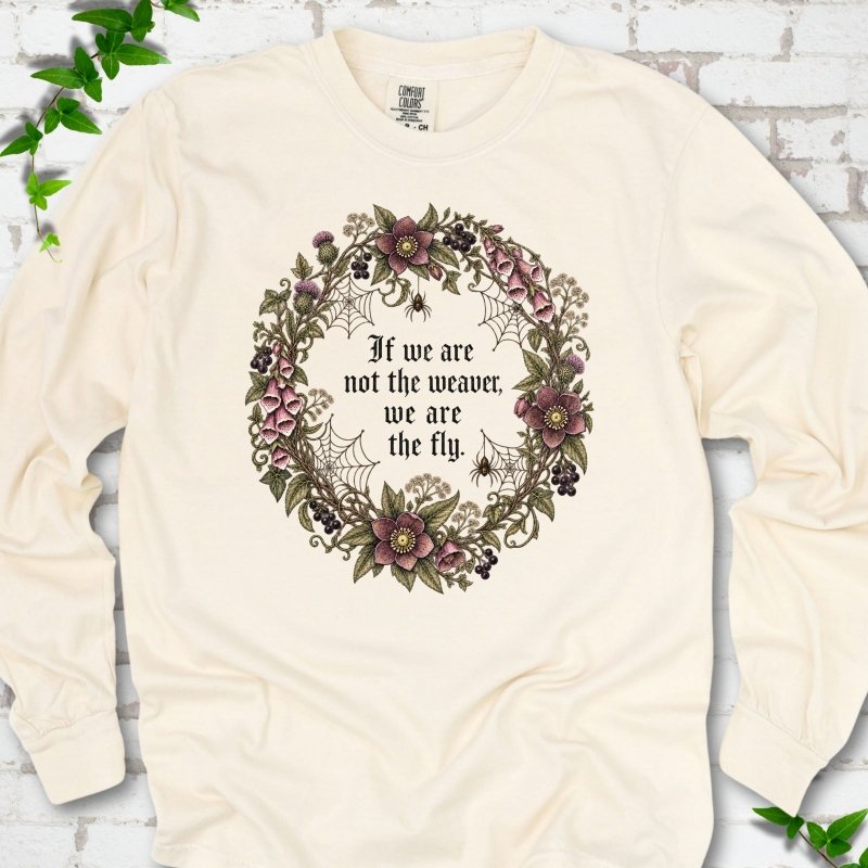 Ivory long sleeve T-shirt flat-lay mockup with a gothic floral wreath, spider webs and "If we are not the weaver, we are the fly" lettering.