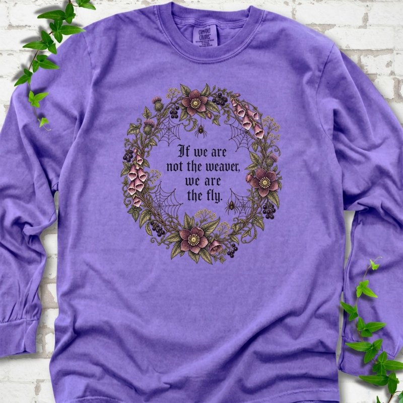 Violet long sleeve T-shirt flat-lay mockup with a gothic floral wreath, spider webs and "If we are not the weaver, we are the fly" lettering.