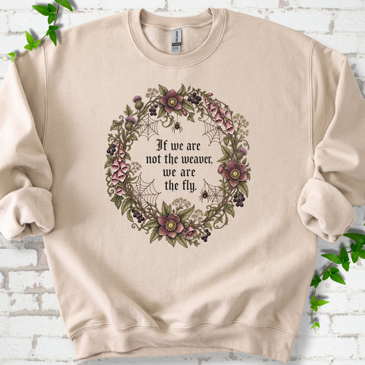 Sand sweatshirt flat-lay mockup with a gothic floral wreath, spider webs and "If we are not the weaver, we are the fly" lettering.