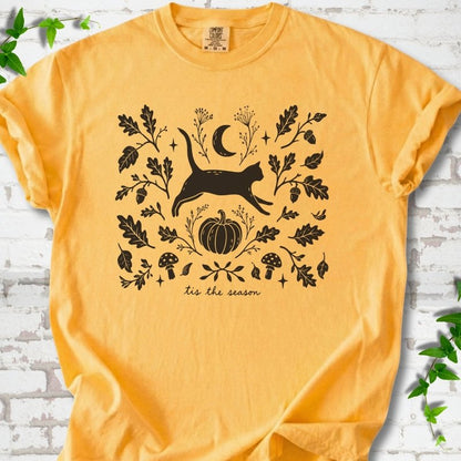 Citrus Comfort Colors® T-shirt flat lay featuring a black cat leaping through autumn oak leaves, acorns, a moon, pumpkin and woodland mushrooms.