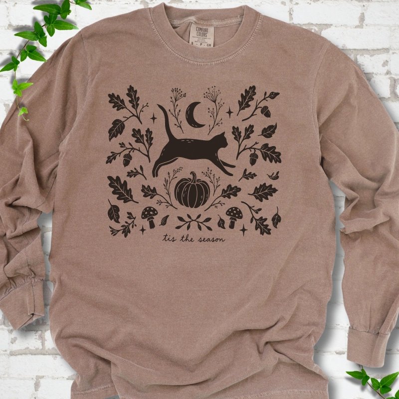 Espresso Comfort Colors® long sleeve T-shirt flat lay featuring a black cat leaping through autumn oak leaves, acorns, a moon, pumpkin and woodland mushrooms.