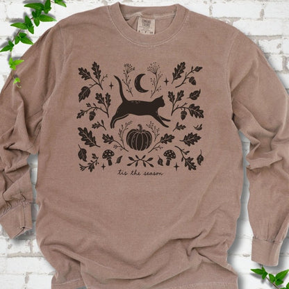 Espresso Comfort Colors® long sleeve T-shirt flat lay featuring a black cat leaping through autumn oak leaves, acorns, a moon, pumpkin and woodland mushrooms.