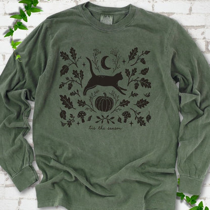 Hemp Comfort Colors® long sleeve T-shirt flat lay featuring a black cat leaping through autumn oak leaves, acorns, a moon, pumpkin and woodland mushrooms.