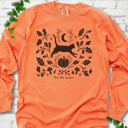Melon Comfort Colors® long sleeve T-shirt flat lay featuring a black cat leaping through autumn oak leaves, acorns, a moon, pumpkin and woodland mushrooms.