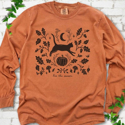 Yam Comfort Colors® long sleeve T-shirt flat lay featuring a black cat leaping through autumn oak leaves, acorns, a moon, pumpkin and woodland mushrooms.