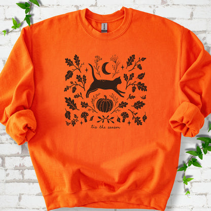 Orange Gildan® 18000 crewneck sweatshirt flat lay featuring a black cat leaping among oak leaves, acorns, a crescent moon, pumpkin and mushrooms.
