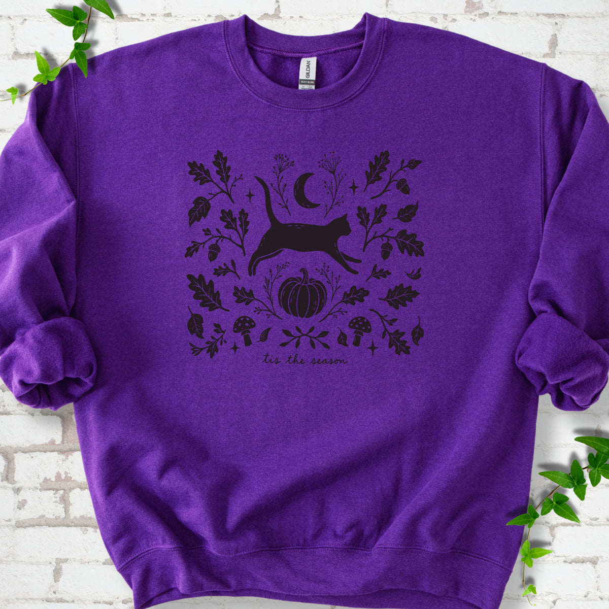 Purple Gildan® 18000 crewneck sweatshirt flat lay featuring a black cat leaping among oak leaves, acorns, a crescent moon, pumpkin and mushrooms.