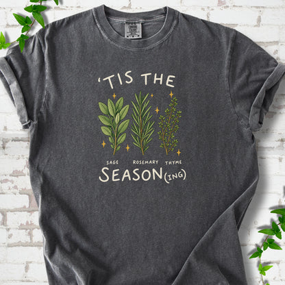 Pepper T-shirt flat lay with ’Tis the Season(ing) lettering, sage, rosemary, thyme and small gold stars.