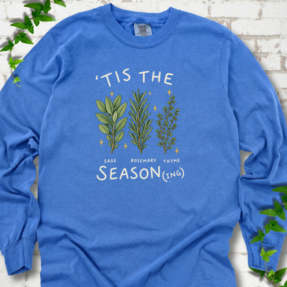 Flo Blue long sleeve T-shirt flat lay with ’Tis the Season(ing) lettering, sage, rosemary, thyme and small gold stars.