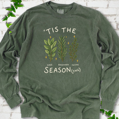 Hemp long sleeve T-shirt flat lay with ’Tis the Season(ing) lettering, sage, rosemary, thyme and small gold stars.