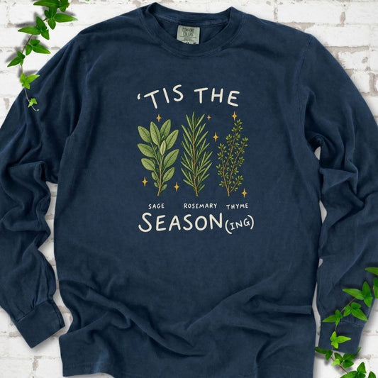 Midnight long sleeve T-shirt flat lay with ’Tis the Season(ing) lettering, sage, rosemary, thyme and small gold stars.