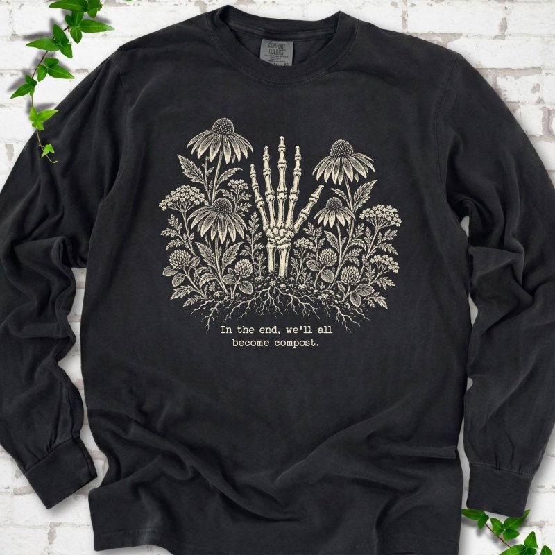 Black Comfort Colors® long sleeve T-shirt featuring a cream botanical skeleton-hand graphic reading In the end, we'll all become compost
