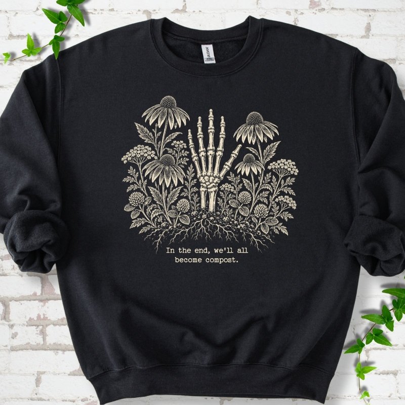 Black classic sweatshirt featuring a cream botanical skeleton-hand graphic reading In the end, we'll all become compost