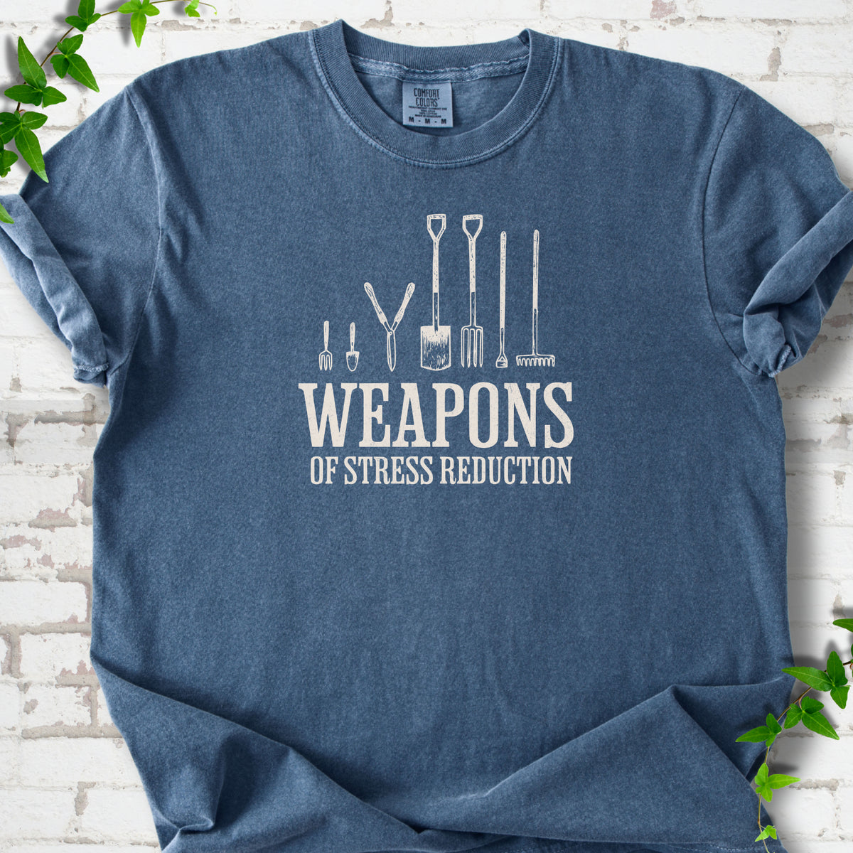 Denim Comfort Colors® T-shirt flat lay featuring garden tools and the words “Weapons of Stress Reduction.”
