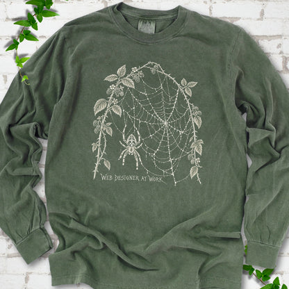 Hemp Comfort Colors® long sleeve T-shirt laid flat, showing a cream spider and intricate web framed by trailing leaves, with “Web designer at work” below.