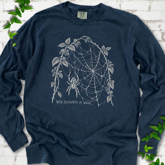 Midnight Comfort Colors® long sleeve T-shirt laid flat, showing a cream spider and intricate web framed by trailing leaves, with “Web designer at work” below.