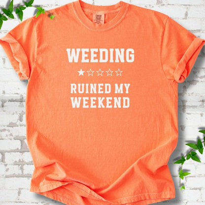 Melon short sleeve T-shirt laid flat on white brick with greenery, showing cream 'Weeding Ruined My Weekend' lettering and a one-star rating on the chest.