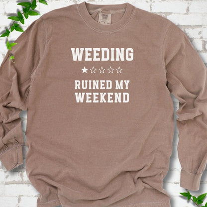 Espresso long sleeve T-shirt laid flat on white brick with greenery, showing cream 'Weeding Ruined My Weekend' lettering and a one-star rating on the chest.