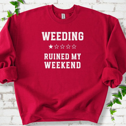 Cardinal Red crewneck sweatshirt laid flat on white brick with greenery, showing cream 'Weeding Ruined My Weekend' lettering and a one-star rating on the chest.