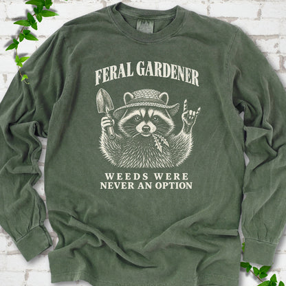 Hemp long sleeve tee laid flat, showing a cream raccoon in a straw hat holding a trowel, with "Feral Gardener" and "Weeds Were Never an Option" lettering.