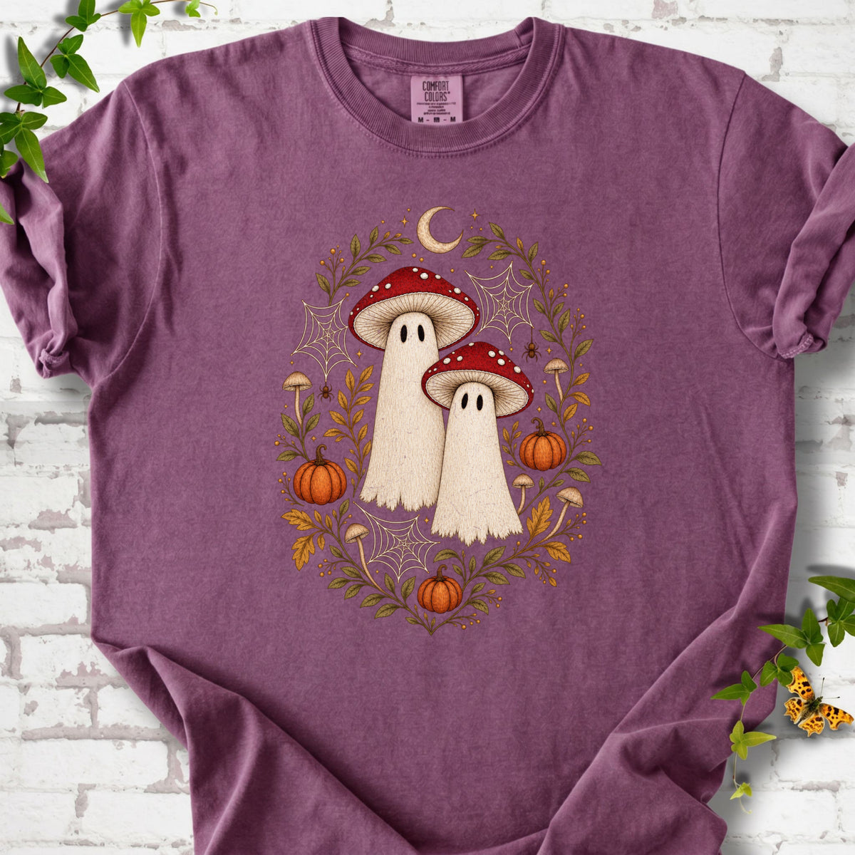 Berry Comfort Colors® T-shirt laid flat, showing two cream ghosts wearing red mushroom caps, surrounded by small pumpkins, autumn leaves and a crescent moon.