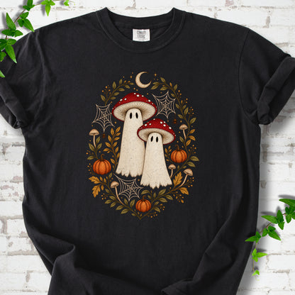 Black Comfort Colors® T-shirt laid flat, showing two cream ghosts wearing red mushroom caps, surrounded by small pumpkins, autumn leaves and a crescent moon.