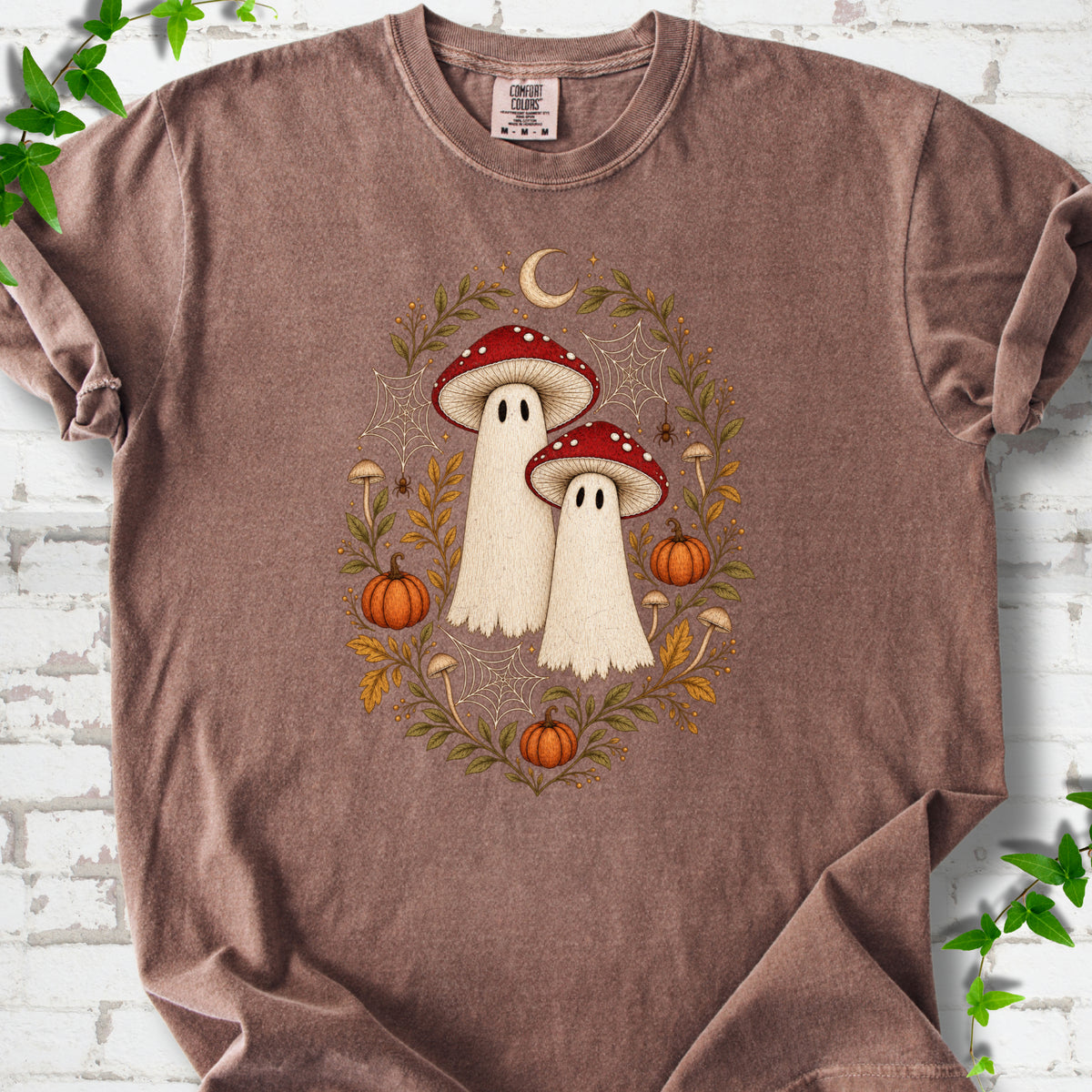 Espresso Comfort Colors® T-shirt laid flat, showing two cream ghosts wearing red mushroom caps, surrounded by small pumpkins, autumn leaves and a crescent moon.