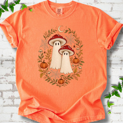 Melon Comfort Colors® T-shirt laid flat, showing two cream ghosts wearing red mushroom caps, surrounded by small pumpkins, autumn leaves and a crescent moon.