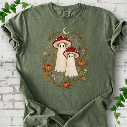 Moss Comfort Colors® T-shirt laid flat, showing two cream ghosts wearing red mushroom caps, surrounded by small pumpkins, autumn leaves and a crescent moon.