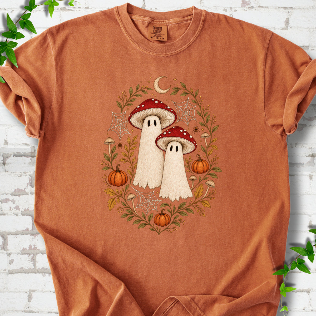 Yam Comfort Colors® T-shirt laid flat, showing two cream ghosts wearing red mushroom caps, surrounded by small pumpkins, autumn leaves and a crescent moon.
