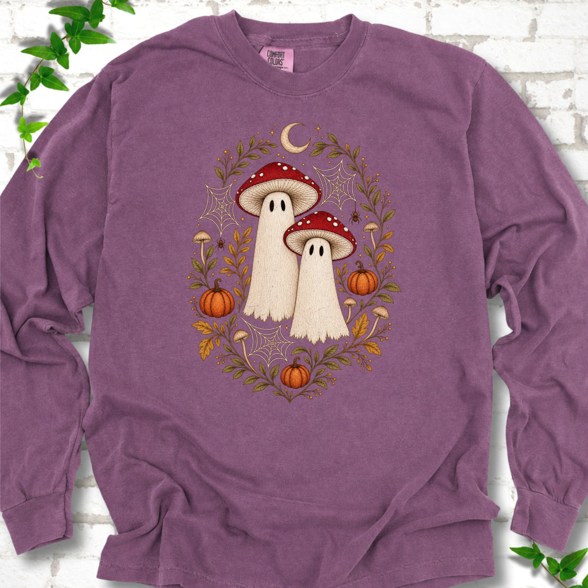 Berry Comfort Colors® long sleeve T-shirt laid flat, showing two cream ghosts wearing red mushroom caps, surrounded by small pumpkins, autumn leaves and a crescent moon.