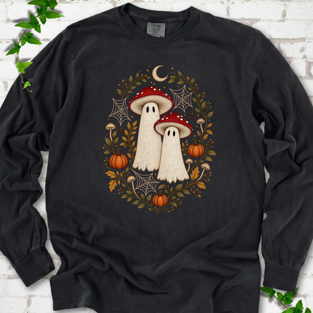 Black Comfort Colors® long sleeve T-shirt laid flat, showing two cream ghosts wearing red mushroom caps, surrounded by small pumpkins, autumn leaves and a crescent moon.