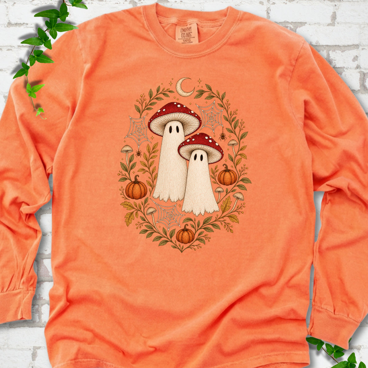 Melon Comfort Colors® long sleeve T-shirt laid flat, showing two cream ghosts wearing red mushroom caps, surrounded by small pumpkins, autumn leaves and a crescent moon.