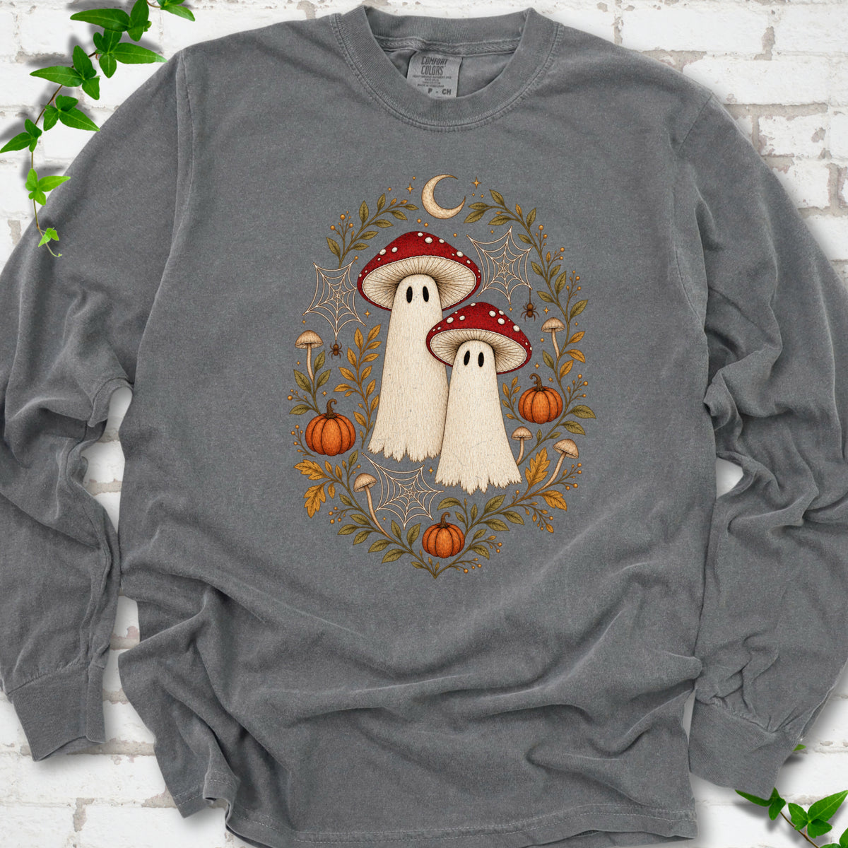 Pepper Comfort Colors® long sleeve T-shirt laid flat, showing two cream ghosts wearing red mushroom caps, surrounded by small pumpkins, autumn leaves and a crescent moon.