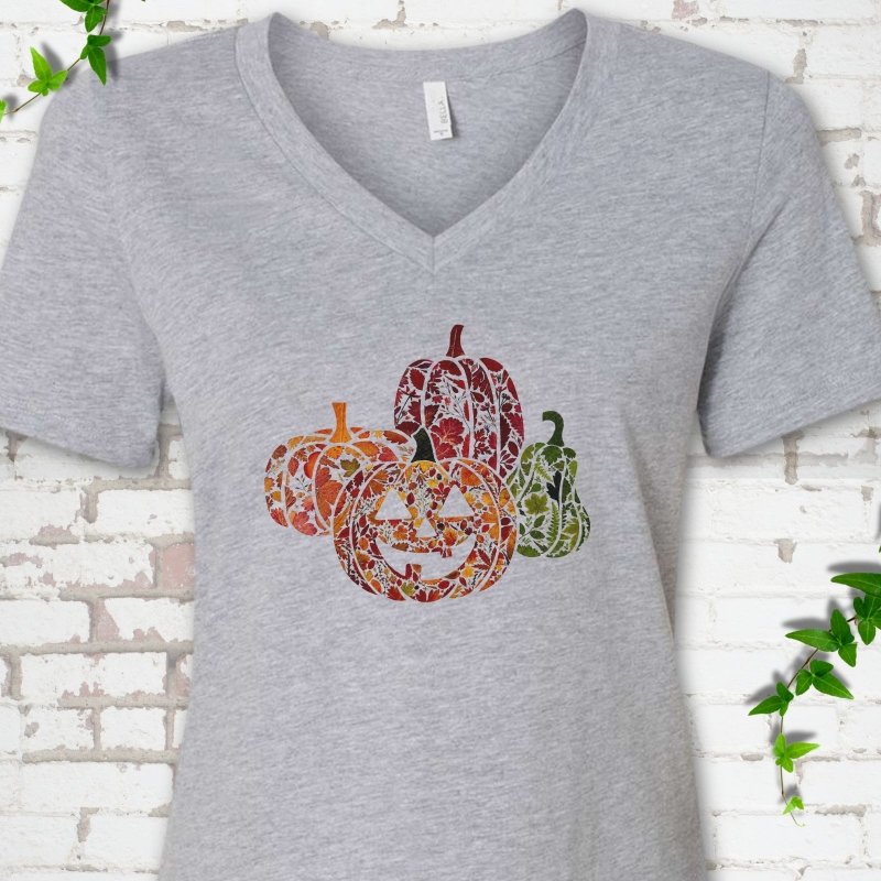 Athletic Heather Bella Canvas® ladies' V-neck T-shirt flat lay featuring four pumpkins filled with colorful autumn leaves, ferns and wildflowers, including one smiling jack-o'-lantern.