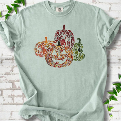 Bay Comfort Colors® T-shirt flat lay featuring four pumpkins filled with colorful autumn leaves, ferns and wildflowers, including one smiling jack-o'-lantern.