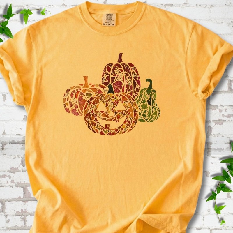 Citrus Comfort Colors® T-shirt flat lay featuring four pumpkins filled with colorful autumn leaves, ferns and wildflowers, including one smiling jack-o'-lantern.