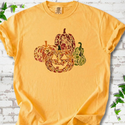 Citrus Comfort Colors® T-shirt flat lay featuring four pumpkins filled with colorful autumn leaves, ferns and wildflowers, including one smiling jack-o'-lantern.