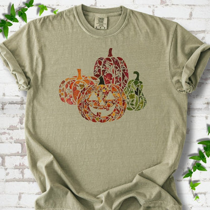 Khaki Comfort Colors® T-shirt flat lay featuring four pumpkins filled with colorful autumn leaves, ferns and wildflowers, including one smiling jack-o'-lantern.