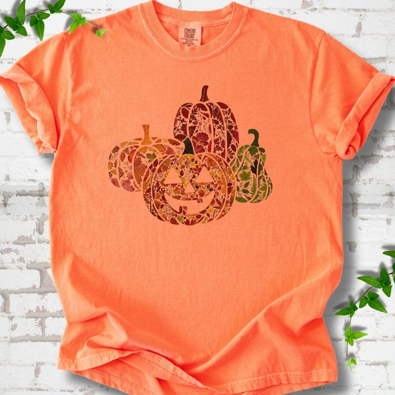 Melon Comfort Colors® T-shirt flat lay featuring four pumpkins filled with colorful autumn leaves, ferns and wildflowers, including one smiling jack-o'-lantern.
