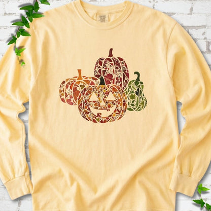 Butter Comfort Colors® long sleeve T-shirt flat lay featuring four pumpkins filled with colorful autumn leaves, ferns and wildflowers, including one smiling jack-o'-lantern.