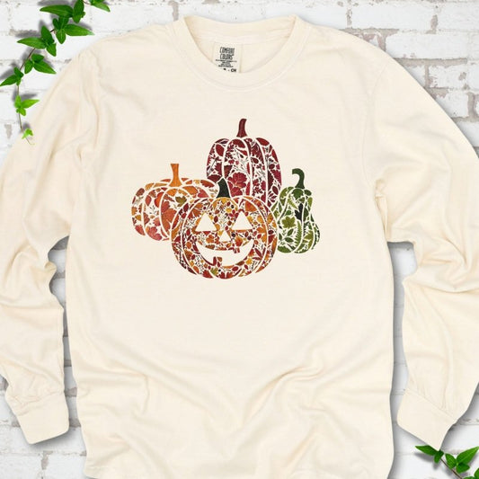 Ivory Comfort Colors® long sleeve T-shirt flat lay featuring four pumpkins filled with colorful autumn leaves, ferns and wildflowers, including one smiling jack-o'-lantern.