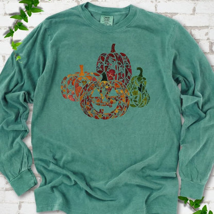 Light Green Comfort Colors® long sleeve T-shirt flat lay featuring four pumpkins filled with colorful autumn leaves, ferns and wildflowers, including one smiling jack-o'-lantern.