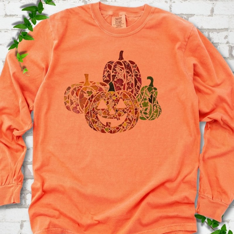 Melon Comfort Colors® long sleeve T-shirt flat lay featuring four pumpkins filled with colorful autumn leaves, ferns and wildflowers, including one smiling jack-o'-lantern.
